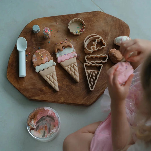 Child playing with ice cream-themed cookies on a wooden board.